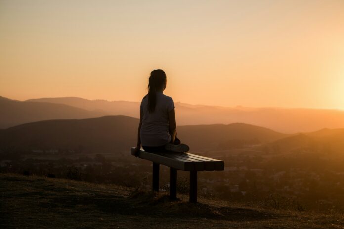 Photo by Sage Friedman woman sitting on bench over viewing mountain