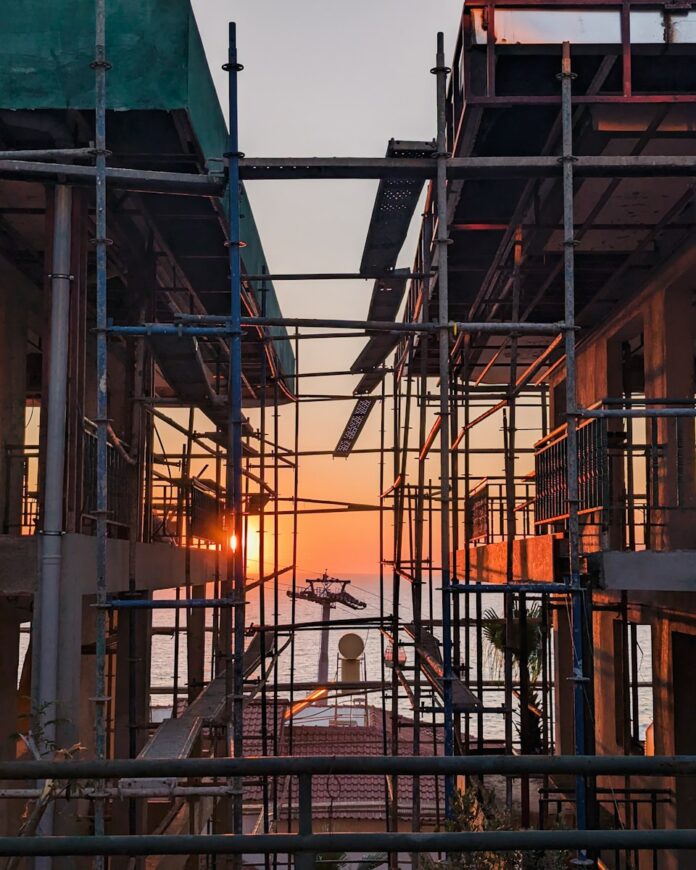 Photo by David Kuvaev scaffolding surrounding a building with the sun setting in the background