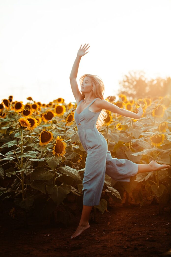 Photo by Blake Cheek close up photography of woman dancing beside sunflower field during golden hour