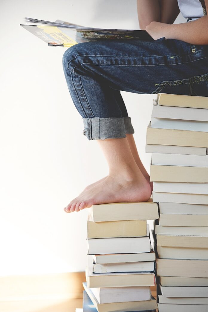 Photo by Gaelle Marcel person sitting on stack of books while reading
