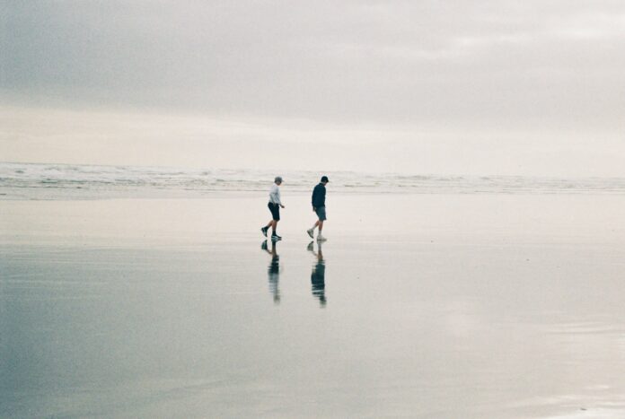 Photo by Charles Cheng two person walking at beach during daytime
