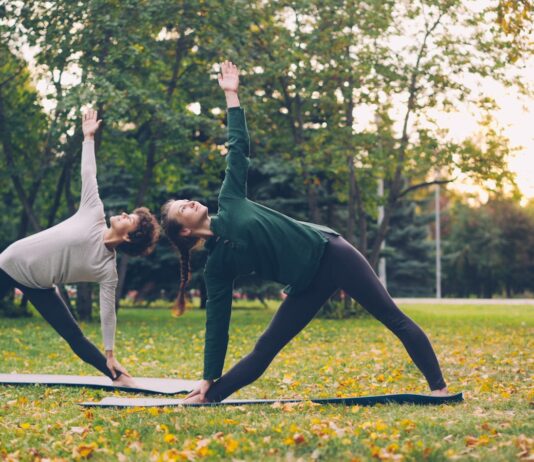 일과 삶의 경계가 흐려지는 시대의 회복 루틴: 직장인 스트레스와 건강 Two women practicing yoga in a park.